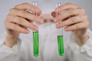 Close-up of hands holding test tubes with green liquid in a laboratory setting.
