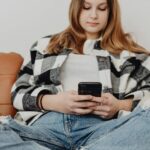 Teenage girl sitting on couch, engrossed in her smartphone, showcasing a relaxed lifestyle.