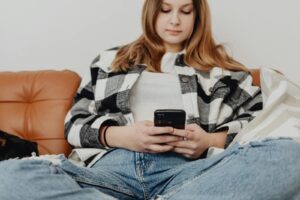 Teenage girl sitting on couch, engrossed in her smartphone, showcasing a relaxed lifestyle.