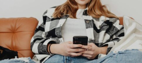 Teenage girl sitting on couch, engrossed in her smartphone, showcasing a relaxed lifestyle.