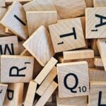 Pile of wooden Scrabble tiles displaying various letters and numbers.