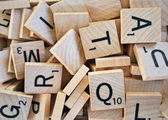 Pile of wooden Scrabble tiles displaying various letters and numbers.