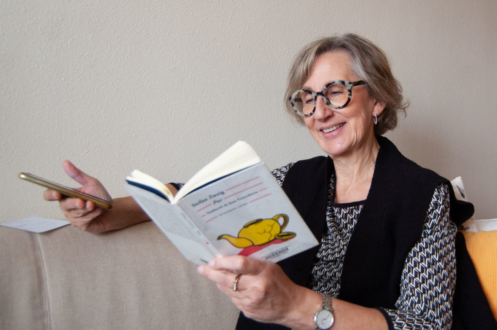 Marta Jove, voluntaria en A Cau d'Orella, sentada en el sofá de su casa, leyendo una novela por teléfono.
