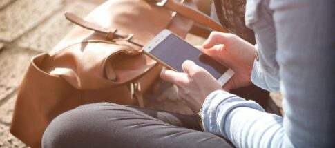 Woman sitting with smartphone and brown bag in sunlight.